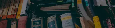 Dimly lit stacks of old books, including titles such as "The Newcomes," "Memoirs of a Field-Marshal" and "Tales After Supper"