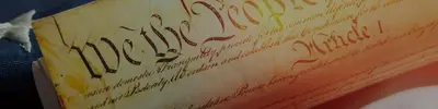 Close-up of the U.S. Constitution parchment showing "We the People" and "Article I" in script.