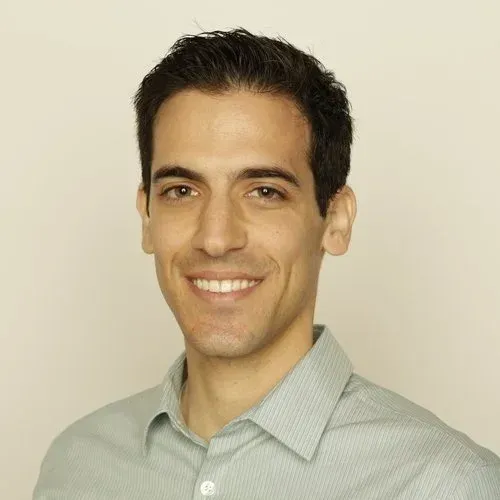 Smiling man with short dark hair in a light gray striped collared shirt against a plain background