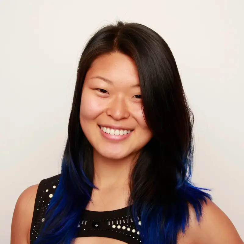 Smiling young woman with long black hair dyed blue at the ends, wearing a sleeveless black top