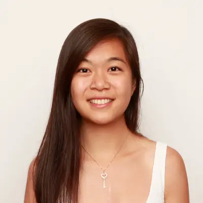 Smiling young woman with long dark hair wearing a white top and a key pendant necklace