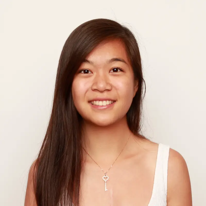 Smiling young woman with long dark hair wearing a white top and a key pendant necklace