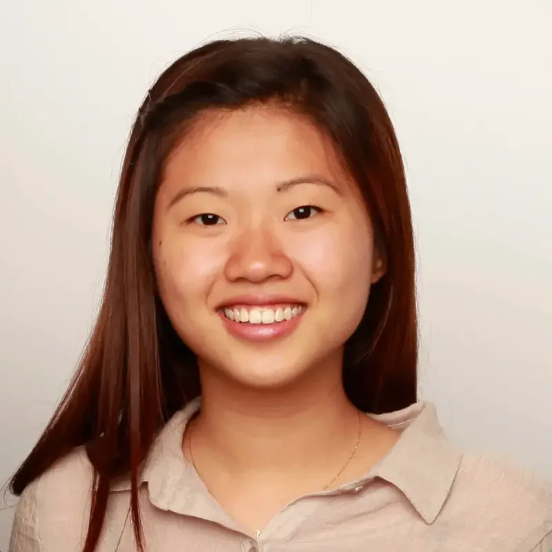 Smiling young woman with long dark hair wearing a beige collared shirt, in a portrait against a plain background
