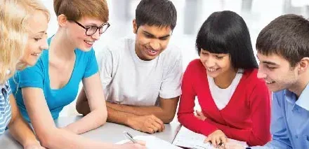 Five smiling students gathered around a table, working together on notes and papers