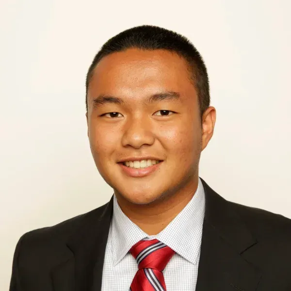 Smiling young man in a dark suit, checked shirt and red striped tie against a plain background