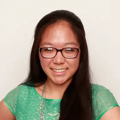 Smiling young woman with long dark hair, glasses, a green lace top and pearl necklace