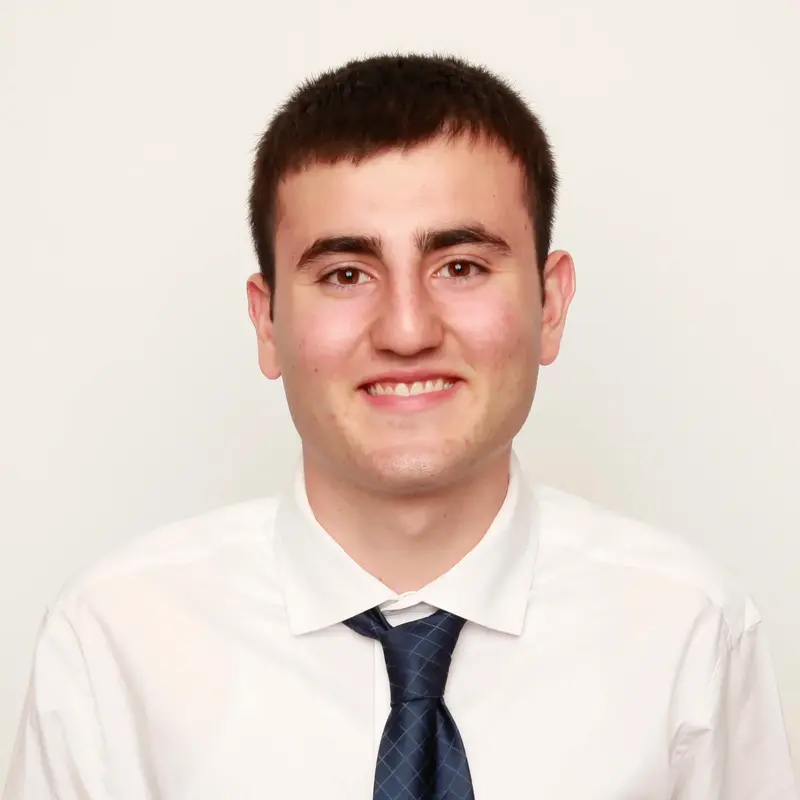Smiling young man with short dark hair in a white dress shirt and navy patterned tie
