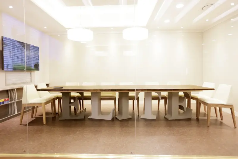 Conference room with a long wooden table on "ELITE" letter bases, white chairs, pendant lights and a wall-mounted screen.