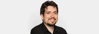 Smiling man with dark hair, goatee and black collared shirt against a plain white background