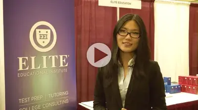 Video thumbnail of a smiling woman in a black blazer standing beside an "Elite Educational Institute" banner at an education fair booth.