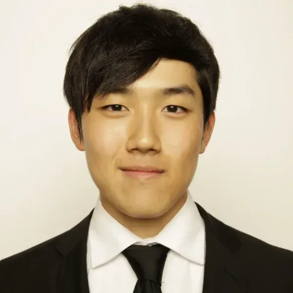 Smiling young man in a black suit, white shirt and black tie against a plain background