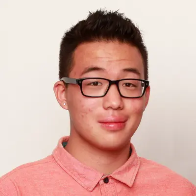 Smiling young man with short dark hair, black-framed glasses and a salmon-colored collared shirt