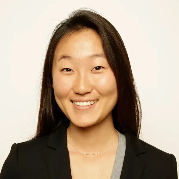 Smiling young woman with long dark hair wearing a black blazer and thin necklace