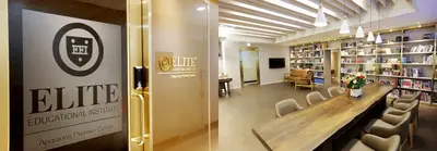 "ELITE EDUCATIONAL INSTITUTE Apgujung Premier Center"가 새겨진 유리 출입문과 책장 및 긴 원목 테이블이 놓인 학습 라운지 전경입니다.