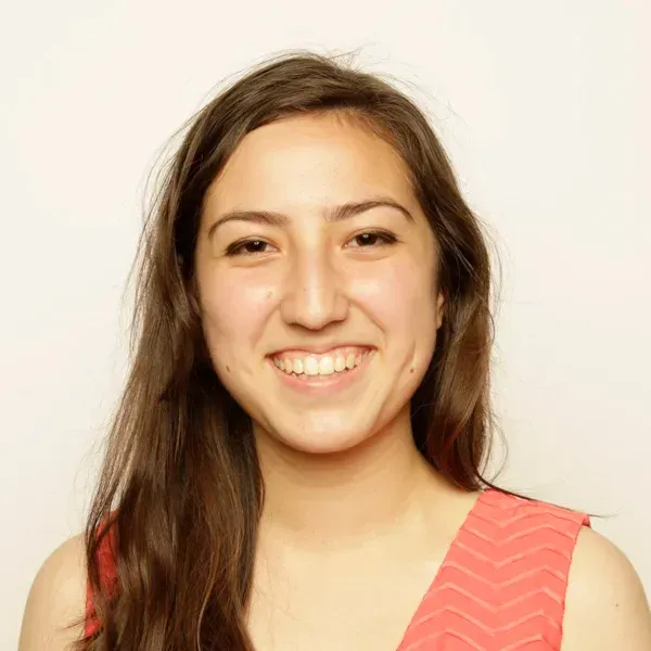 Smiling young woman with long brown hair wearing a coral chevron-patterned top, against a plain background