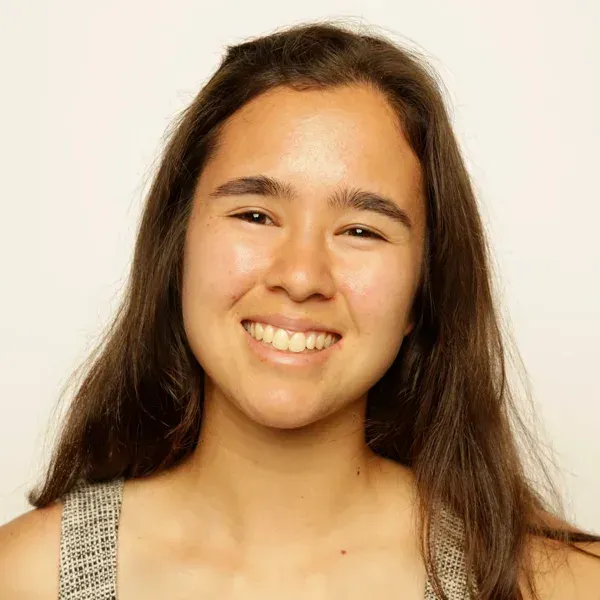 Smiling young woman with long brown hair in a sleeveless top, against a plain light background