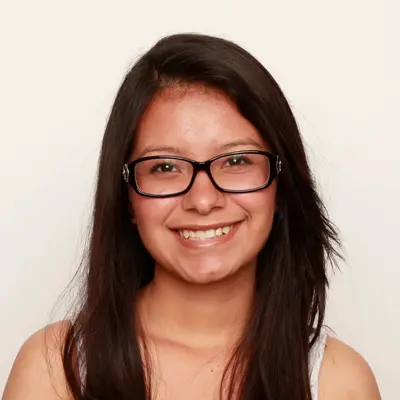 Smiling student with long dark hair and black-framed glasses in a portrait against a plain background