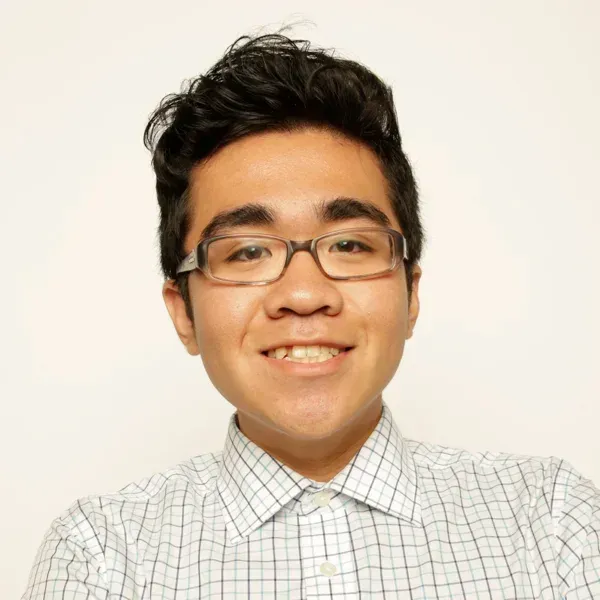 Smiling young man with glasses and dark wavy hair wearing a checked button-down shirt