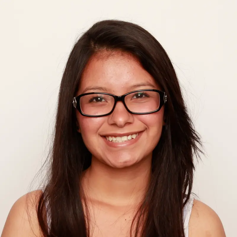 Smiling young woman with long dark hair and black-framed glasses against a plain light background
