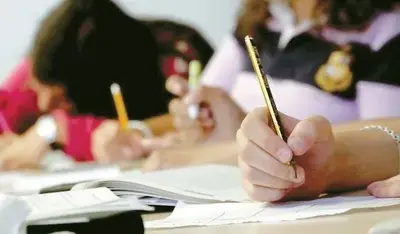 책상에 앉아 연필로 종이와 공책에 글을 쓰고 있는 학생들