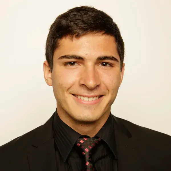 Smiling young man in a black suit and patterned red tie posing for a headshot