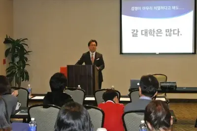 연단에 선 강연자가 '경쟁이 아무리 치열하다고 해도… 갈 대학은 많다.'라는 슬라이드 옆에서 학부모 청중에게 강연하는 모습입니다.
