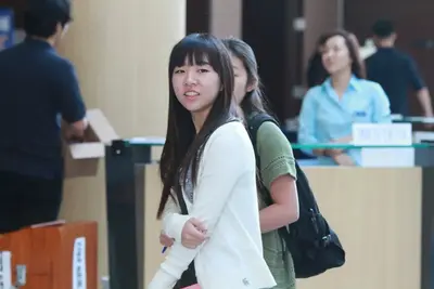 A smiling student in a white cardigan turns toward the camera while walking past a reception desk at an event.