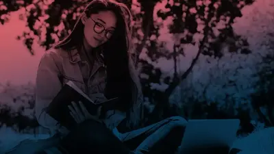 A student in glasses reading a book outdoors under the trees