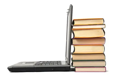 An open laptop viewed from the side, its screen leaning against a tall stack of hardcover books