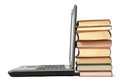 An open laptop viewed from the side, its screen leaning against a tall stack of hardcover books