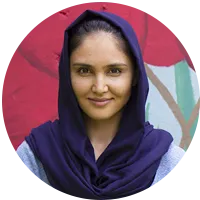 A smiling young woman in a dark blue headscarf, photographed in a circular frame against a colorful mural