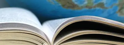 An open book with fanned pages in front of a blurred world globe