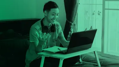 A student waving at his laptop during an online class at home