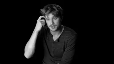 Black-and-white portrait of a young man with his hand in his hair, looking uncertain against a dark background