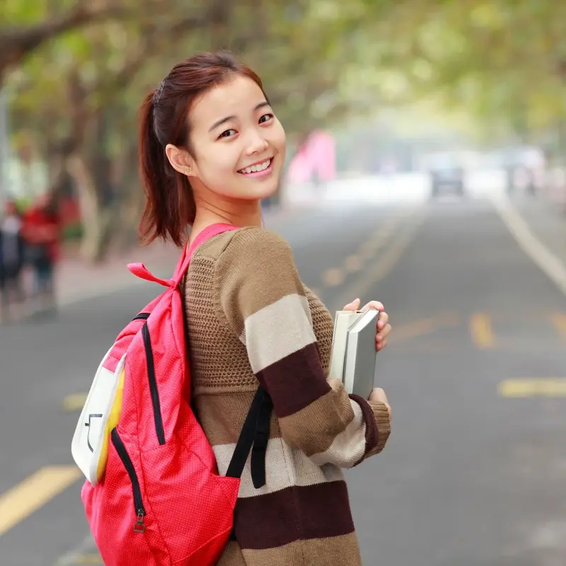 A smiling student with a red backpack, holding her books