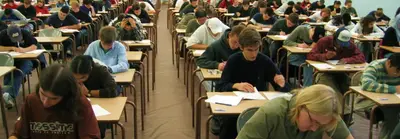 Rows of students seated at individual desks in a large hall, writing an exam.