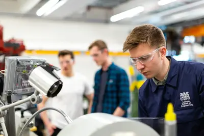 Engineering students in safety glasses working at a machine in a university workshop