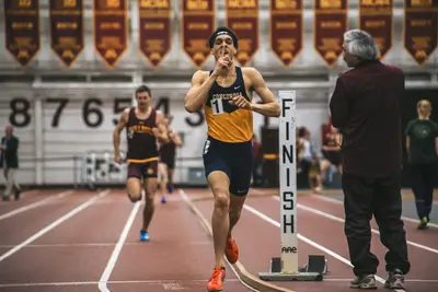 A runner in a Concordia singlet sprints past a FINISH marker on an indoor track as another athlete trails behind.