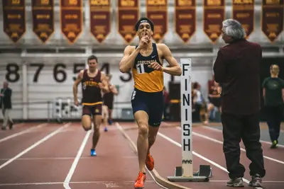 A runner in a Concordia singlet sprints past a FINISH marker on an indoor track as another athlete trails behind.