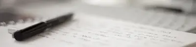 A black pen resting on a page of handwritten notes on a desk